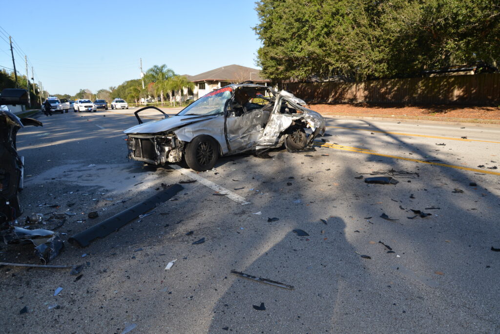 Silver vehicle crashed in the middle of the road surrounded by debris