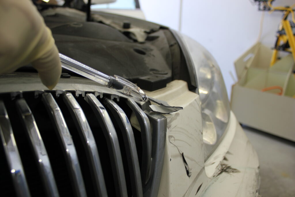 A hand with latex glove holding a pen pointing to a car grille