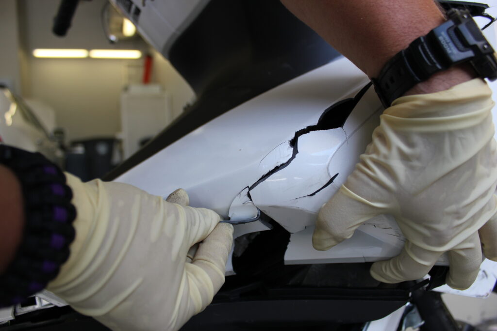 Hands with latex gloves manipulating a piece of broken car bumper